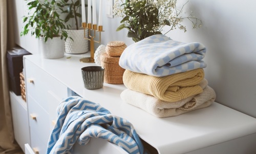 pastel clothes on top of a dresser with green plants in the background
